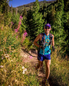 A runner in an OAR singlet smiles as they run along a nature trail.