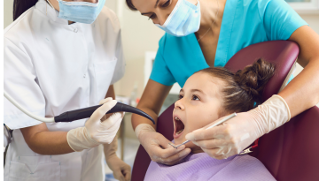 A child is at the dentist, mouth open as the dentist and hygienist check their teeth.