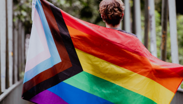 A person holds the LGBTQIA+ flag behind them.